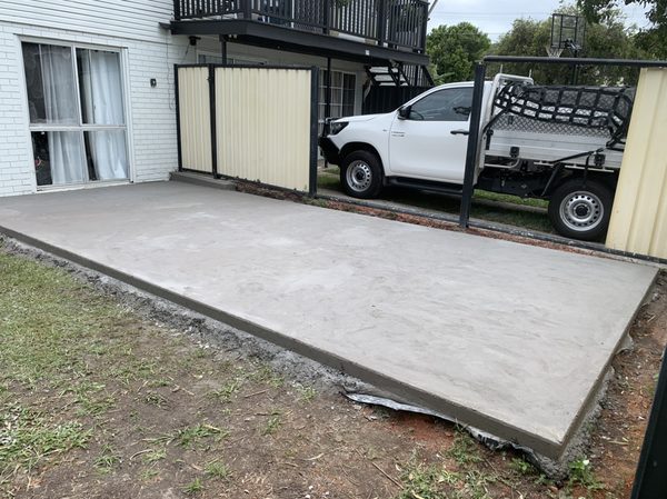 Backyard concrete slab beside a house, with a ute parked in the background