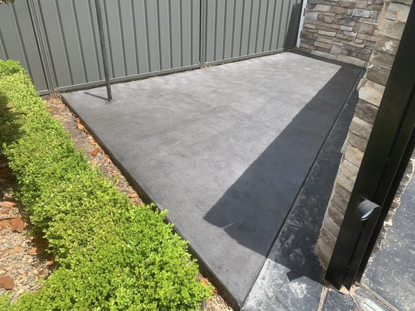 Charcoal concrete side courtyard slab beside a hedge