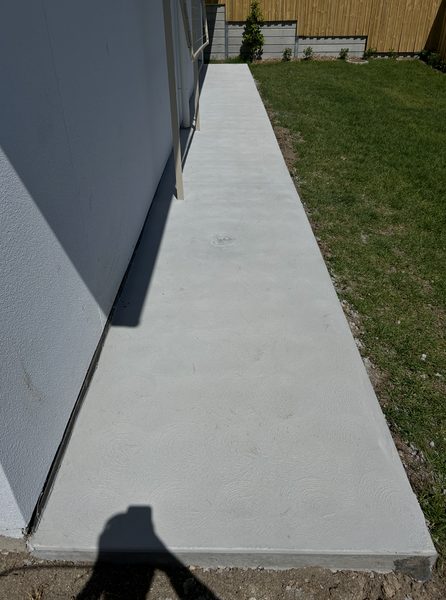 Long concrete side path with a swirl finish beside a house and lawn